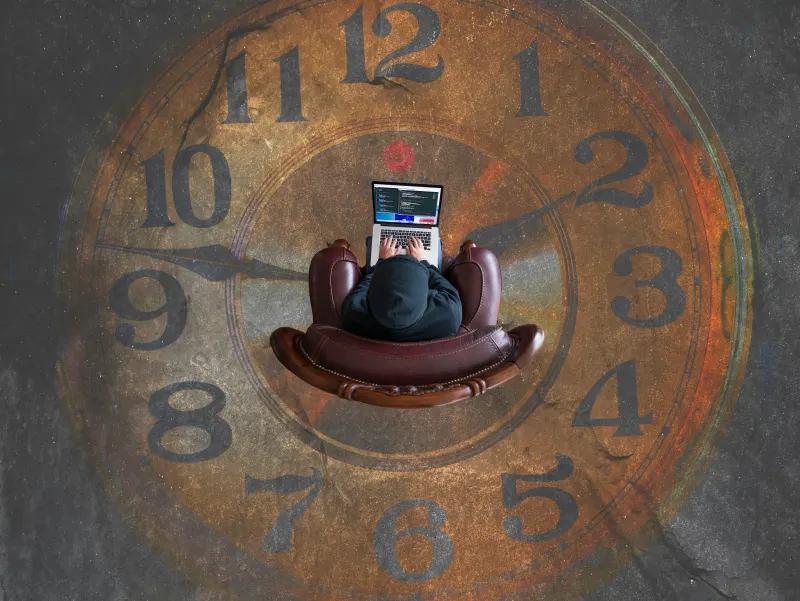 A desk clock sitting next to a laptop and a coffee mug.